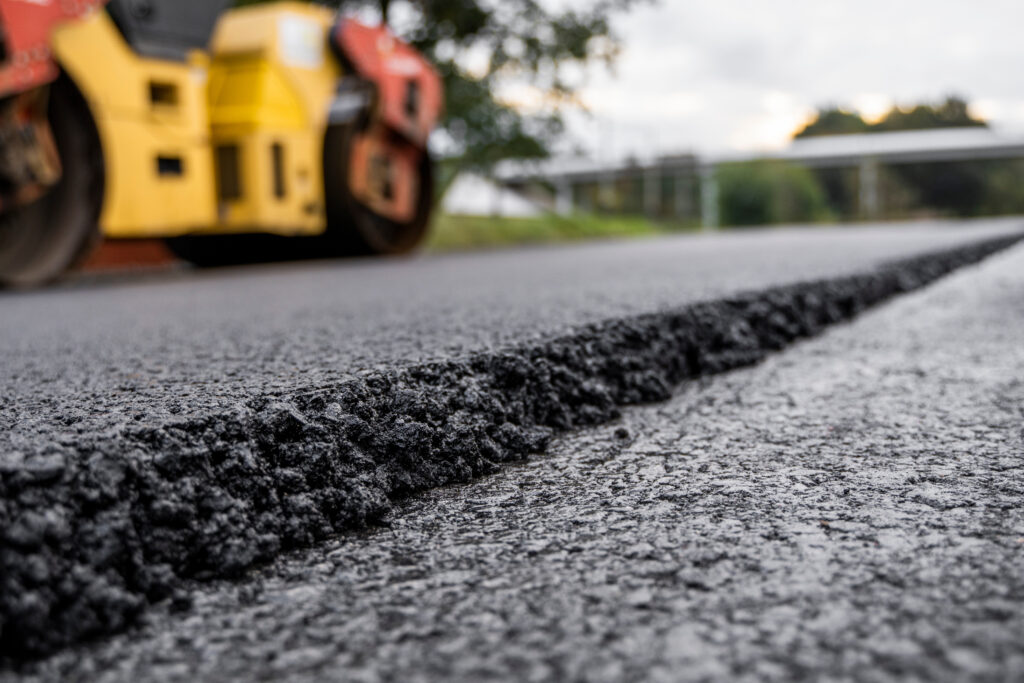 Asphalt road roller with heavy vibration roller compactor press new hot asphalt on the roadway on a road construction site. Heavy Vibration roller at asphalt pavement working. Repairing.